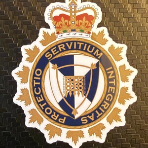 May include: A circular emblem with a crown at the top, featuring a blue and white checkered design, surrounded by a gold border with the words "Servitium Integritas" and "Protectio" in a blue ring. Gold maple leaf accents.