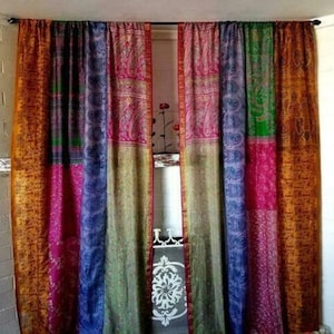 Puede incluir: Cortinas de patchwork coloridas con una variedad de patrones y colores, incluyendo rosa, azul, verde y dorado. Las cortinas cuelgan de una barra negra y parecen estar hechas de una tela suave y fluida. El diseño es bohemio y ecléctico.