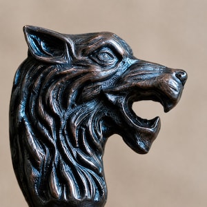 Peut inclure: Sculpture en bronze représentant une tête de loup, avec des détails de fourrure complexes et une gueule ouverte. La sculpture a une finition métallique foncée et est placée sur un fond neutre. Tête de loup artistique.