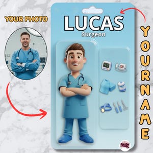 Op de afbeelding: Een lichtblauw speelgoedfiguur van een chirurg genaamd Lucas, met gekruiste armen, draagt een stethoscoop en operatiekleding. De verpakking bevat medische instrumenten en een foto van een persoon in operatiekleding. Tekst: "Surgeon" en "Your Name".