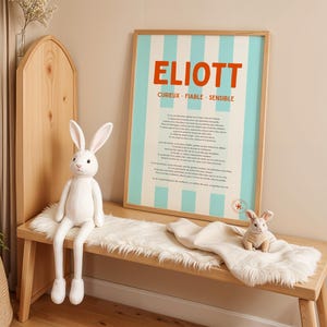 Op de afbeelding: Een houten bank met een witte imitatiebont en twee witte pluchen konijnen. Een ingelijste poster met de naam "ELIOTT" in oranje letters en blauwe strepen hangt aan de muur. De poster bevat ook de woorden "CURIUEUX - FIABLE - SENSIBLE".