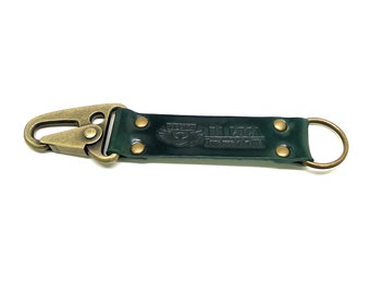 May include: A dark green leather key chain with a brass hook and a brass ring. The leather has the text "DA LIGA" embossed on it.
