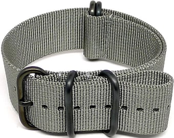 Könnte beinhalten: Ein graues Nylon-Uhrenarmband mit schwarzer Hardware. Das Armband hat eine Schließe und zwei Schlaufen.