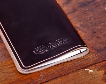May include: A brown leather notebook with a stitched edge and a logo embossed on the cover that reads "The Daily Connoisseur".