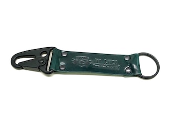 May include: A dark green leather keyring with a black metal clip and a round ring. The keyring has the text "DA LIGA" embossed on it.