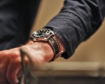 May include: A silver wristwatch with a black face and a brown leather strap. The watch has a date window and a rotating bezel.