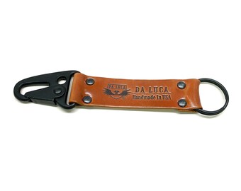 May include: A brown leather key chain with a black metal clip and a ring. The keychain has the text "DA LUCA Handmade in USA" embossed on it.
