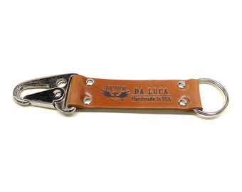 May include: A brown leather key chain with a silver hook and a silver ring. The leather strap has the text "DA LUCA Handmade in USA" embossed on it.