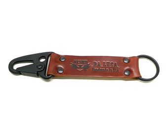 May include: A brown leather key chain with a black metal clip and a black metal ring. The keychain has the text "DA LUCA Handmade in USA" embossed on it.
