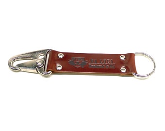 May include: A brown leather key chain with a silver hook and a silver ring. The keychain has the text "DA LUCA Handmade in USA" embossed on it.
