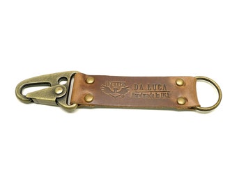 May include: A brown leather keychain with a brass key ring and a brass clip. The leather strap has a logo that says "DA LUCA Handmade in USA".
