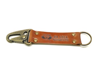 May include: A brown leather key chain with a brass hook and a brass ring. The key chain has the text "DA LUCA Handmade in USA" embossed on it.