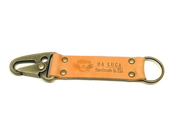 May include: A tan leather key chain with a brass hook and a brass ring. The keychain has the text "DA LUCA Handmade in USA" embossed on it.