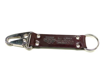 May include: A brown leather key chain with a silver metal hook and a ring. The leather strap has the text "DA LUCA Handmade in USA" embossed on it.
