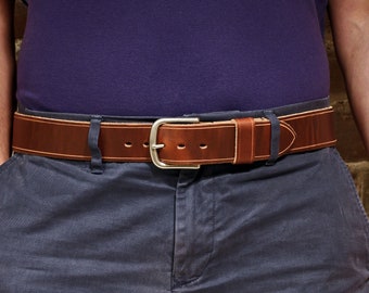 May include: A brown leather belt with a silver buckle. The belt is worn around the waist of a person wearing a purple shirt and blue trousers.