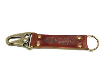 May include: A brown leather key chain with a brass hook and a brass ring. The leather strap has the text "DA LUCA Handmade in USA" embossed on it.