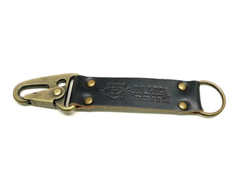 May include: A black leather key chain with a brass hook and a brass ring. The leather strap has the text "DA LUCA handmade in USA" embossed on it.