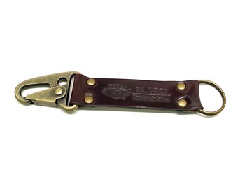 May include: A brown leather key chain with a brass hook and a brass ring. The leather strap has the text "DA LUCA Handmade in USA" embossed on it.