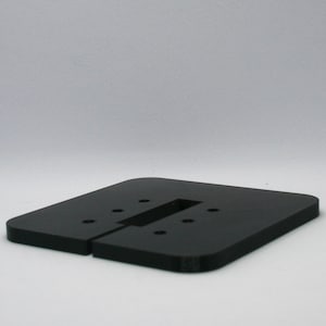 Peut inclure: Une base carrée plate en plastique noir aux coins arrondis, dotée d'une découpe rectangulaire centrale et de six petits trous circulaires disposés symétriquement sur la surface. L'objet présente une finition mate lisse et un profil bas.