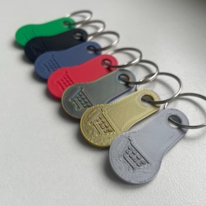 Puede incluir: Una colección de llaveros con fichas de carrito de la compra de colores. Los llaveros son de varios colores, incluyendo verde, negro, azul, rojo, gris y dorado. Cada llavero tiene un diseño de carrito de la compra y un llavero plateado.