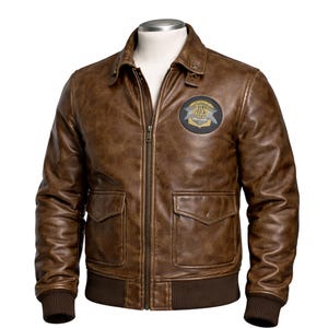 May include: Brown leather jacket with a zip-up front, two front pockets, and a patch on the upper left chest. The jacket has a ribbed knit hem and cuffs. The leather has a distressed appearance.