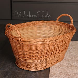 May include: An oval-shaped wicker basket with two arched handles. The basket is a natural light brown colour. The text "Wicker Side" is written on the side of the basket.