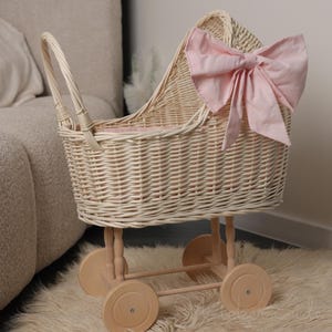 May include: A wicker doll's pram with a large pink bow. The pram features a woven basket design, wooden wheels, and a handle. The interior is lined with pink fabric. A delightful toy for children.