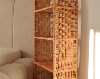 May include: A tall, arched-top wicker bookshelf with four shelves. The natural-toned bookcase is made of woven wicker and stands against a neutral-colored wall. The shelves are open and ready for display.