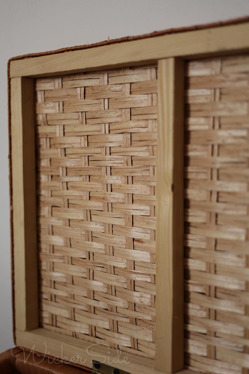 Pode incluir: Close-up de uma cesta de vime tecida em tons castanhos claros. A cesta tem formato retangular, com uma moldura de madeira clara. A trama intrincada do vime &eacute; claramente vis&iacute;vel, criando uma superf&iacute;cie texturizada.