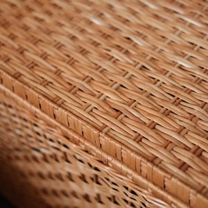 Pode incluir: Close-up de uma superf&iacute;cie de vime tecido, mostrando um padr&atilde;o detalhado de fios entrela&ccedil;ados. O vime tem um tom castanho claro e quente, com textura e profundidade vis&iacute;veis. As palavras "Wicker Side" s&atilde;o vis&iacute;veis no canto inferior esquerdo.