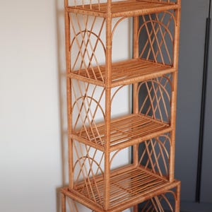 May include: A tall, freestanding wicker shelf unit with an arched top and multiple shelves. The natural brown wicker is woven into a lattice design on the sides and back, creating an open and airy storage solution. The unit has five shelves and is approximately 60 inches tall.