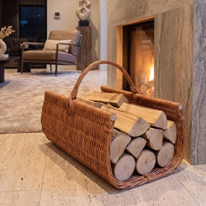 Può includere: Un cesto rettangolare in vimini intrecciato con un unico manico ad arco, riempito con legna da ardere spaccata di colore marrone chiaro. Il cesto presenta una finitura naturale color beige ed è realizzato con sottili rami di salice intrecciati.