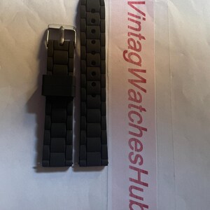 May include: Black watch band with a textured, rectangular pattern. The band has a silver-colored buckle. The text "VintagWatchesHub" is printed on a pink and white label.
