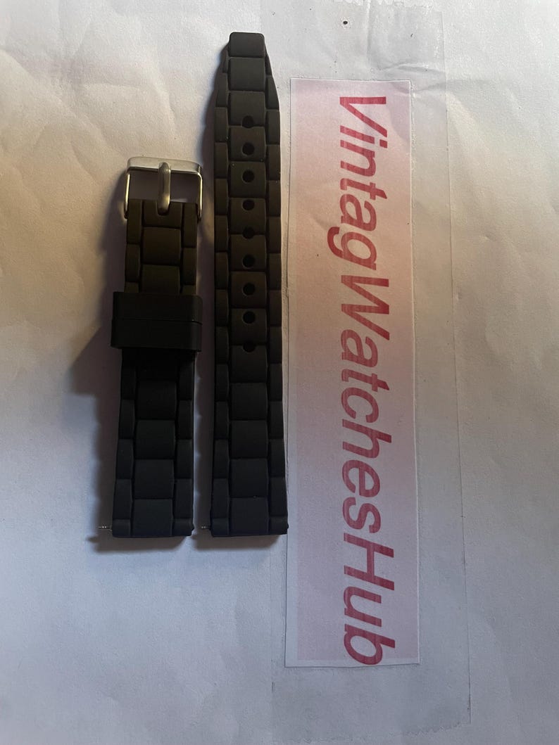 May include: Black watch band with a textured, rectangular pattern. The band has a silver-colored buckle. The text "VintagWatchesHub" is printed on a pink and white label.