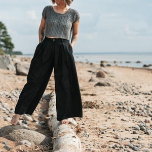 May include: A grey short-sleeved knit top with a cable-knit pattern and a round neckline, paired with black wide-leg trousers featuring a high waist, front pleats, a button closure, and side pockets, creating a coordinated two-piece outfit.