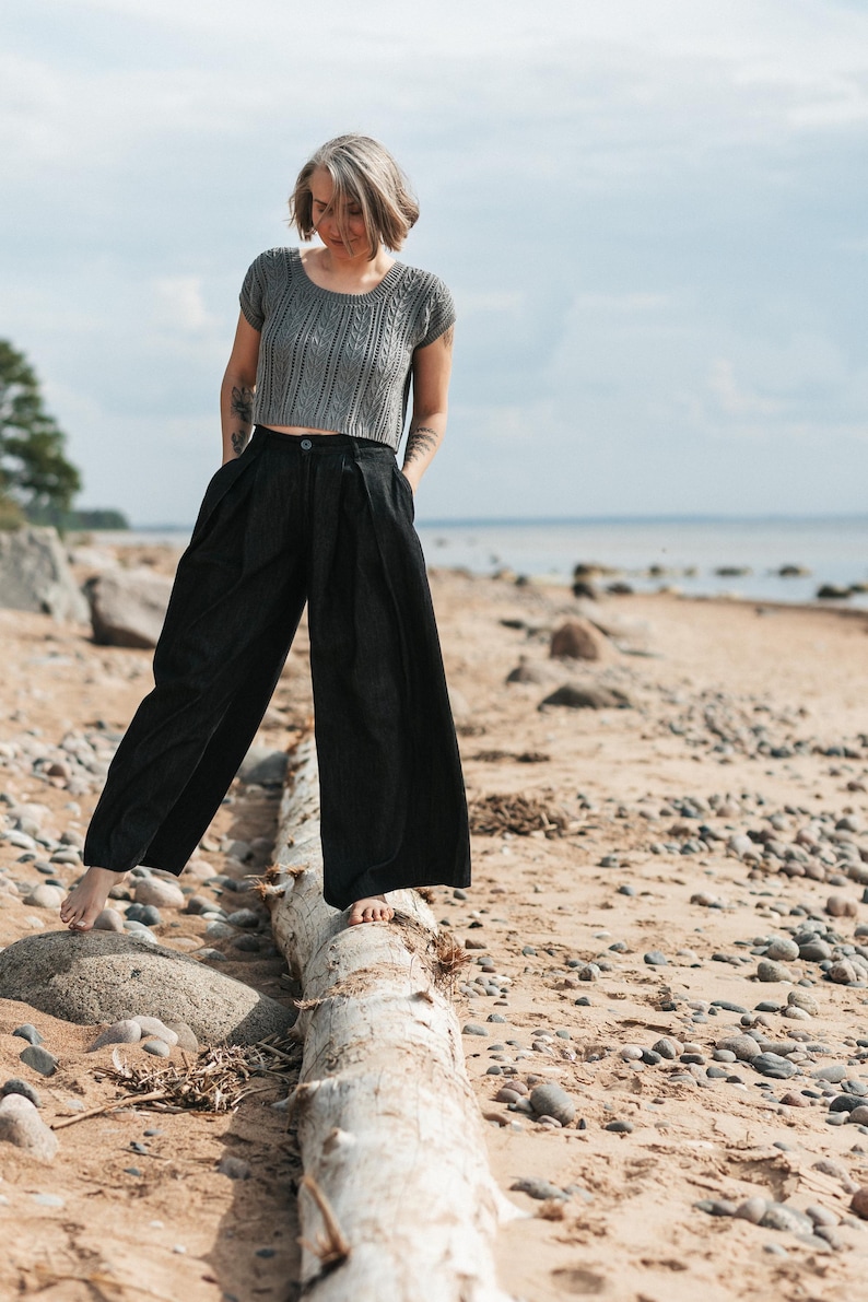 May include: A grey short-sleeved knit top with a cable-knit pattern and a round neckline, paired with black wide-leg trousers featuring a high waist, front pleats, a button closure, and side pockets, creating a coordinated two-piece outfit.