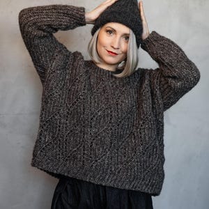 Könnte beinhalten: Ein dunkel anthrazitfarbener Langarmpullover mit strukturiertem Rauten-Zopfmuster, geripptem Rundhalsausschnitt und Bündchen, kombiniert mit einer passenden dunkel anthrazitfarbenen Rippstrickmütze und einer dunkel anthrazitfarbenen Hose.