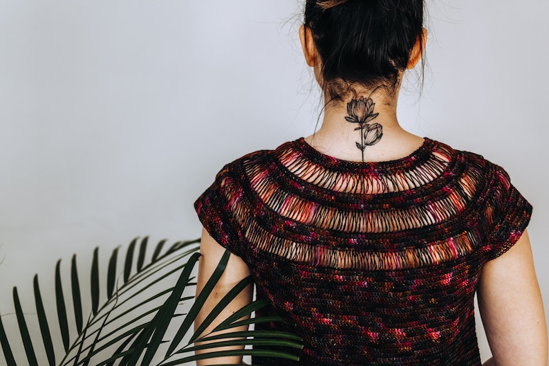 May include: A woman wearing a black and red crochet top with a floral tattoo on the back of her neck.