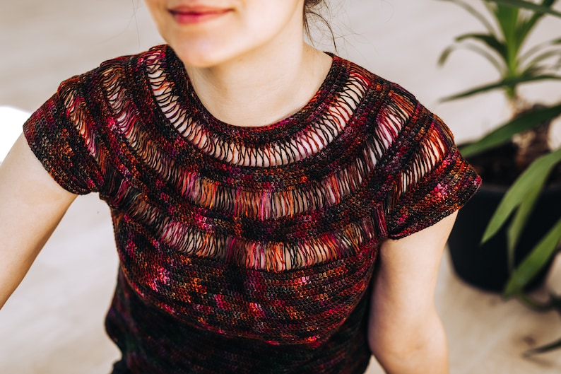 May include: A close-up of a crocheted top with a colorful, multi-colored design. The top has a wide, open neckline and short sleeves.