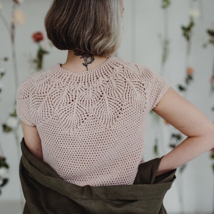May include: A pink crocheted top with a delicate leaf pattern around the neckline and short sleeves.