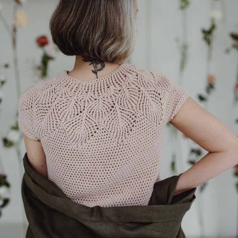 May include: A pink crocheted top with a delicate leaf pattern around the neckline and short sleeves.