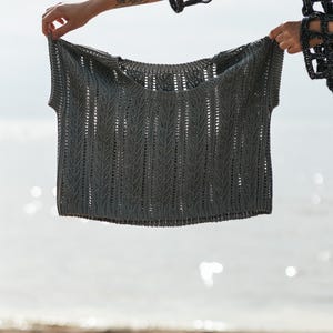 May include: A dark gray knit top featuring a vertical chevron stitch pattern, a wide round neckline, and short sleeves. The garment is constructed with a textured, open-work design that creates a subtle repeating pattern across the entire surface.