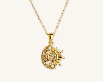 May include: Gold-toned necklace featuring a pendant with a sun and moon design. The sun has radiating rays and the moon is a crescent shape. Both are embellished with small, clear crystals. The chain is delicate and also gold-toned.