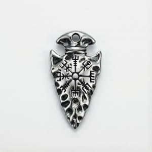 May include: A silver-coloured pendant shaped like an arrowhead. It features a detailed Viking compass design, with a hole for a chain. The surface has a textured, weathered appearance, giving it an antique look.