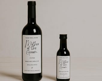 Könnte beinhalten: Zwei schwarze Weinflaschen mit weißen Etiketten. Die Etiketten lauten "Pairs Well With Mother of the Groom" mit Hochzeitsdetails. Eine Flasche ist in voller Größe, die andere ist eine Miniatur.