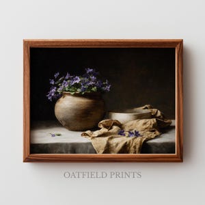 Könnte beinhalten: Ein gerahmter Druck mit einem Stillleben. Eine braune Vase mit lila Blumen steht auf einem Tisch mit einem beigen Tuch. Eine Holzschale und verstreute Blumen sind ebenfalls vorhanden. Der Text "OATFIELD PRINTS" befindet sich unten.
