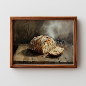 May include: A framed painting depicts a loaf of bread with a slice cut out, resting on a wooden surface. The bread has a golden-brown crust and a light-colored interior. The painting uses a muted color palette with soft lighting.