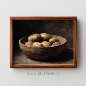 Puede incluir: Una impresión enmarcada que presenta un bodegón de patatas en un cuenco de madera. Las patatas son de varios tonos de marrón y beige, y el cuenco es de madera oscura y rústica. La impresión tiene una estética vintage, con el texto "OATFIELD PRINTS".