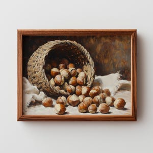Puede incluir: Una pintura de naturaleza muerta representa una cesta de mimbre desbordante de avellanas. Las nueces están esparcidas sobre un paño blanco, con un fondo marrón oscuro. La pintura está enmarcada en un marco de madera oscura.