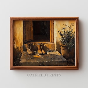 Puede incluir: Una impresión artística enmarcada representa una escena rústica con dos pares de botas en un escalón de piedra frente a una puerta. La obra de arte presenta tonos cálidos y terrosos y una planta en maceta, evocando nostalgia y encanto rural. El texto "OATFIELD PRINTS" está en la parte inferior.